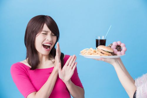 Asian woman resisting junk food being offered to her.
