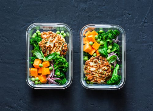 Two containers full of healthy vegetables and grilled chicken.