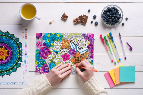 Woman filling colors in an adult coloring book whilst having tea, chocolate and blueberries.