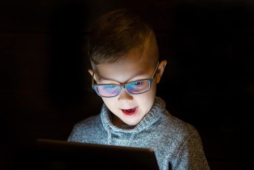 Young boy with spectacles getting amused by his tablet. 