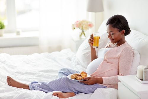 A pregnant African woman having cookies and orange juice in bed.