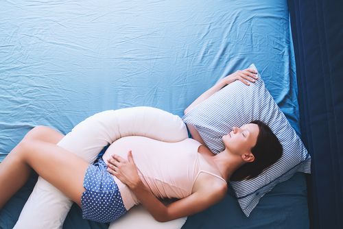 Woman sleeping with a pregnancy pillow.
