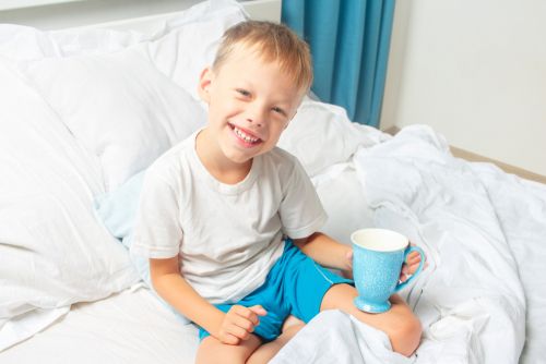 Smiling boy having milk in bed.
